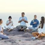 group of people sitting in circle and meditating by the seaside