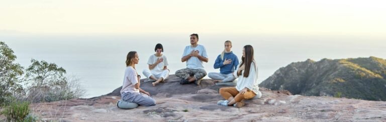 group of people sitting in circle and meditating by the seaside